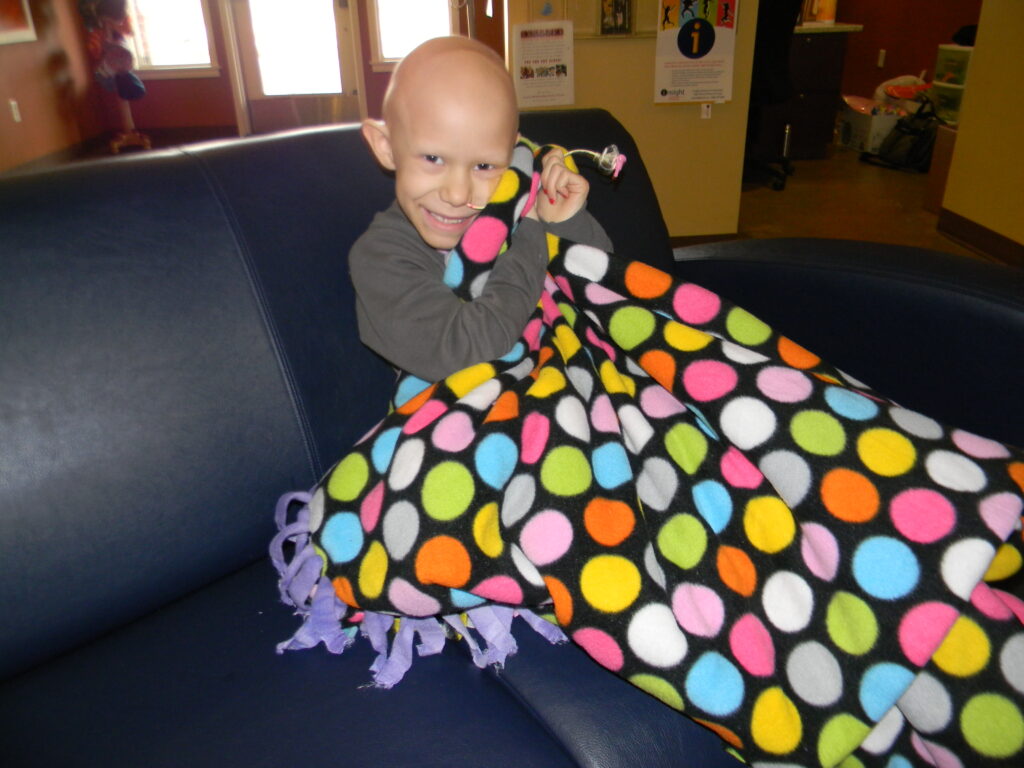 Child smiling, covered in rainbow polka dot blanket.