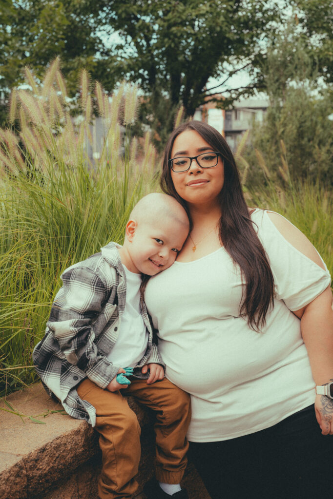 Mother wearing white shirt with her arm around child with bald head.